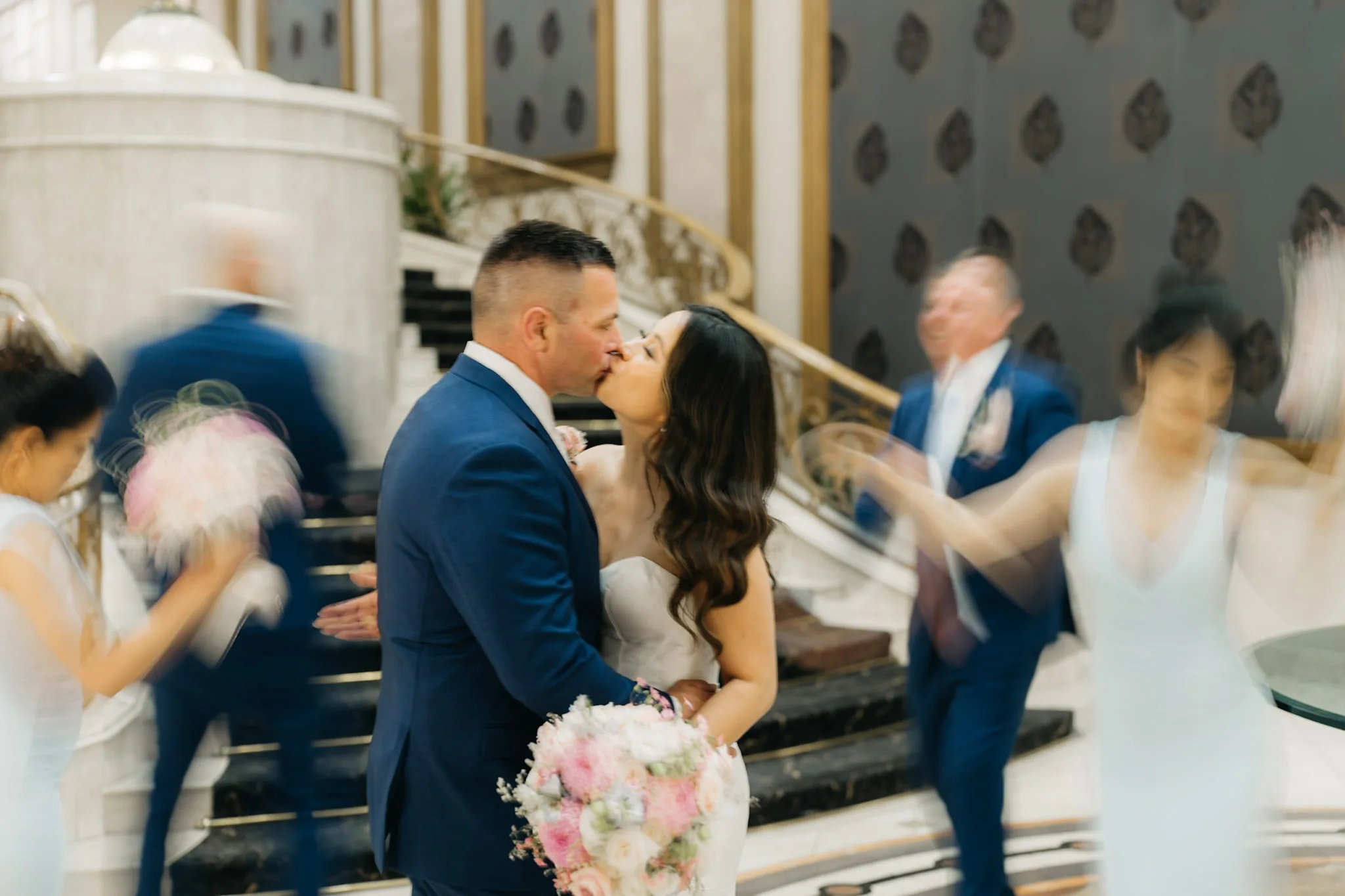 Che and Rob kissing as their wedding party moves around them