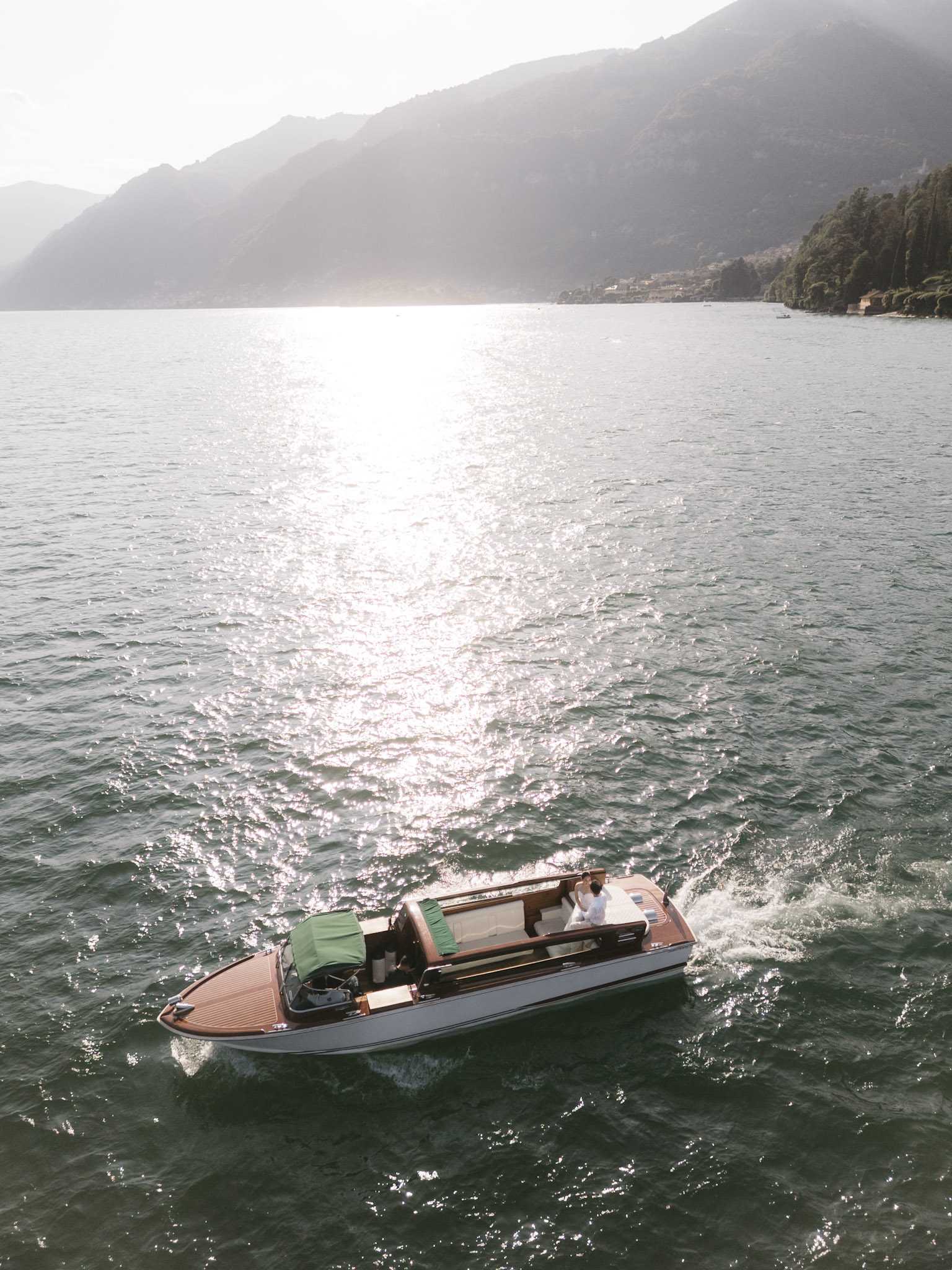 A boat crossing silver water beneath the mountains of Lake Como