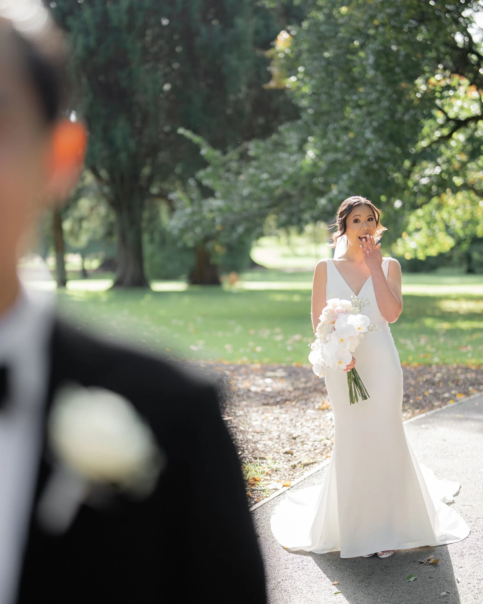 Bride smiling with a hand near her mouth as she approaches the groom in a garden.