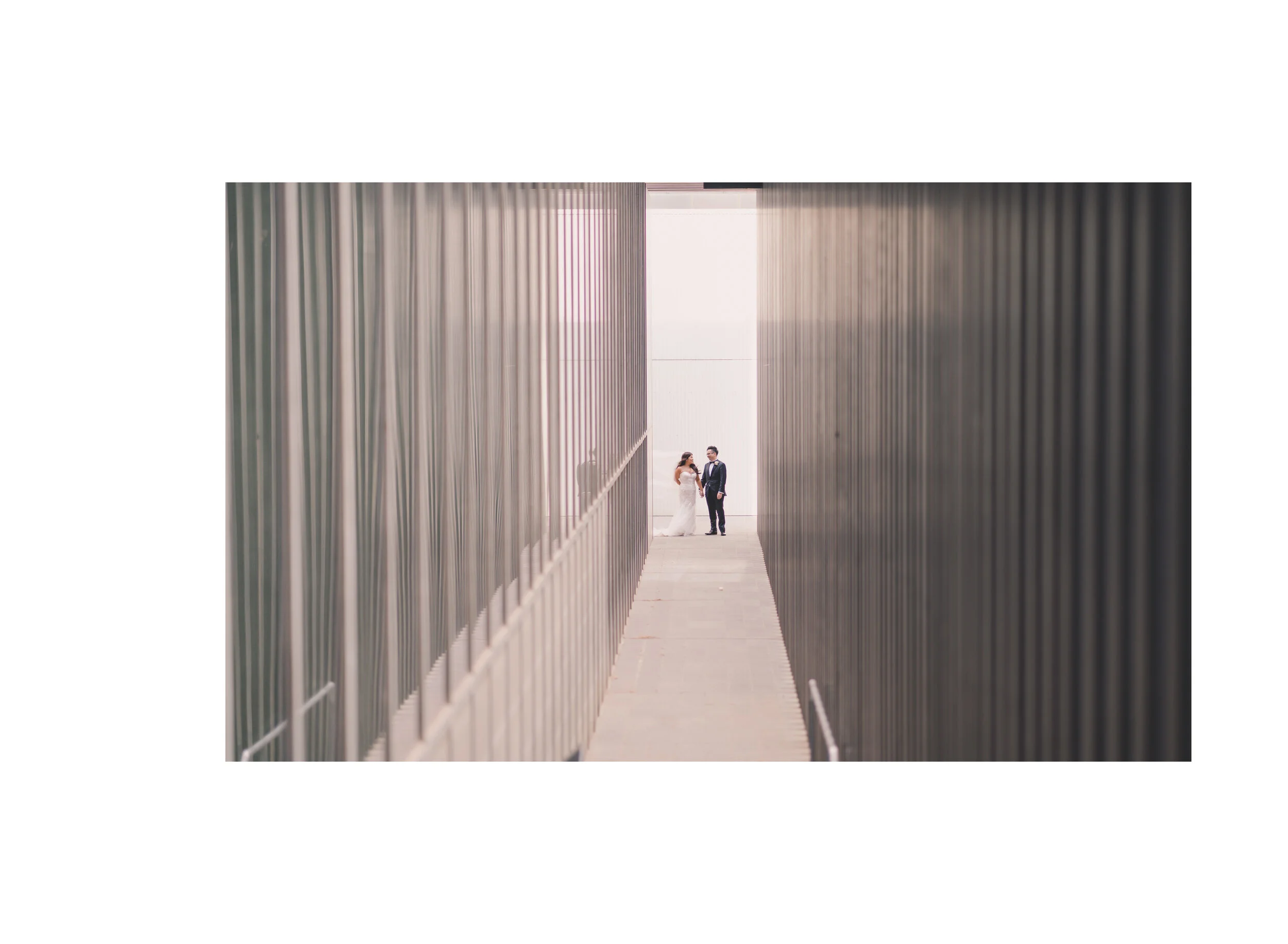Newlyweds framed at the end of a modern architectural walkway