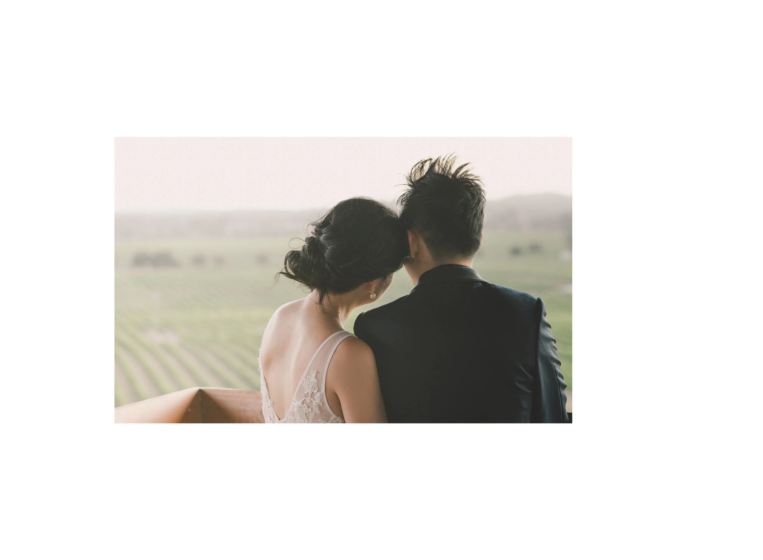Newlyweds resting their heads together above a rural landscape