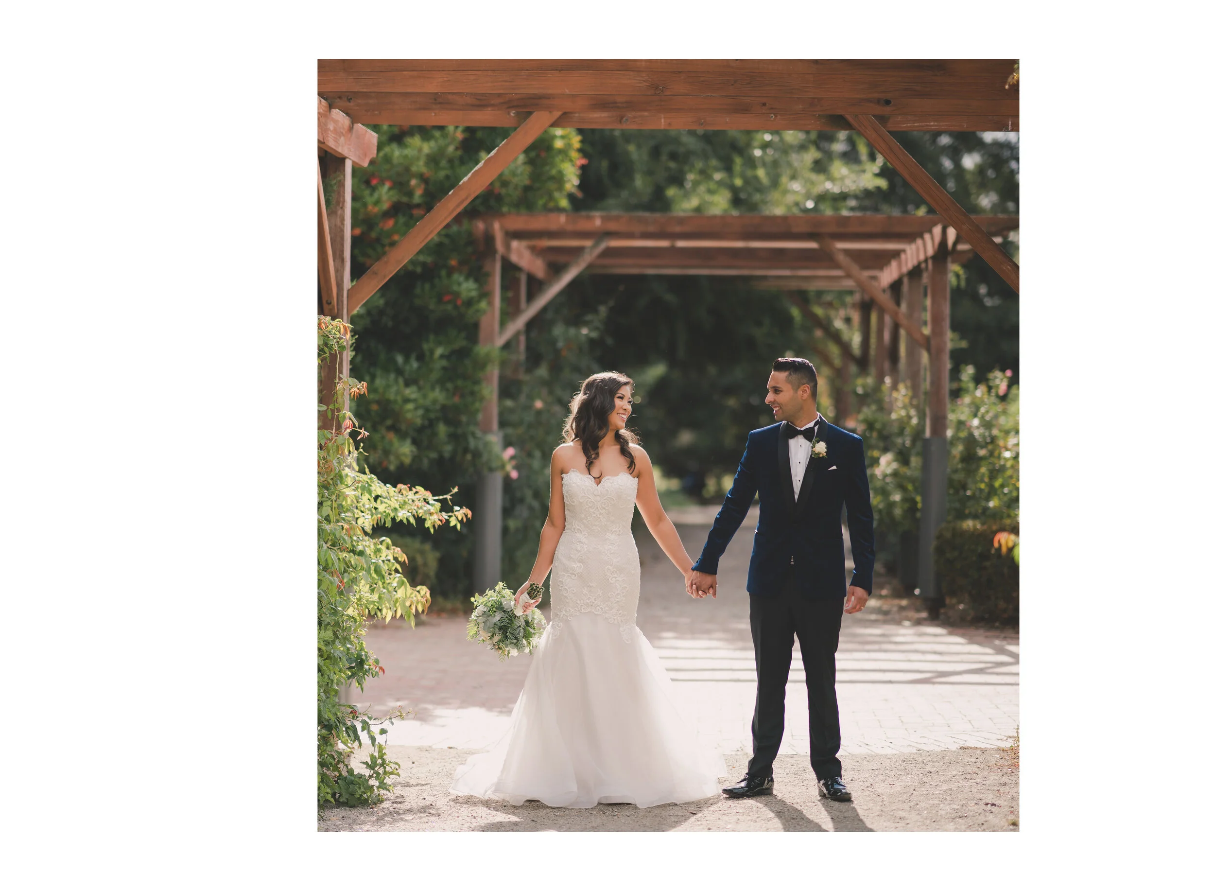 Newlyweds walking hand in hand beneath a timber garden pergola