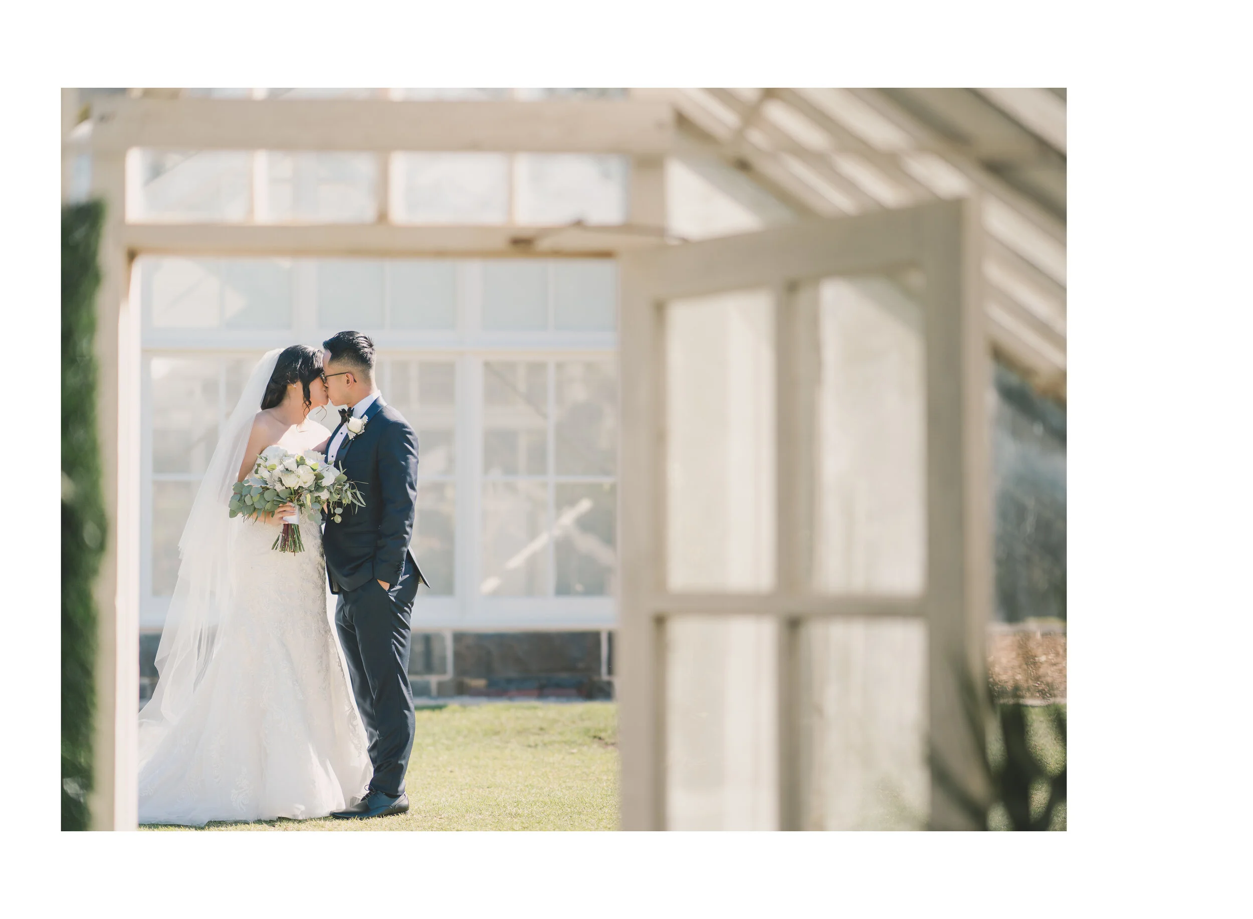 Newlyweds kissing inside a bright glasshouse