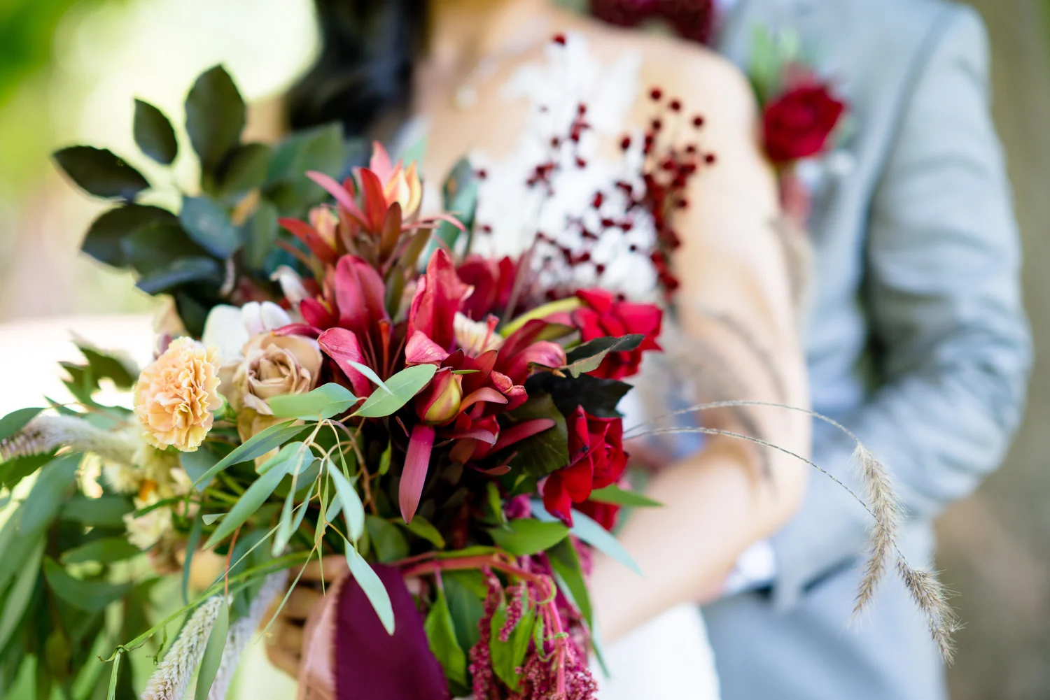 Rich red wedding bouquet held between a couple