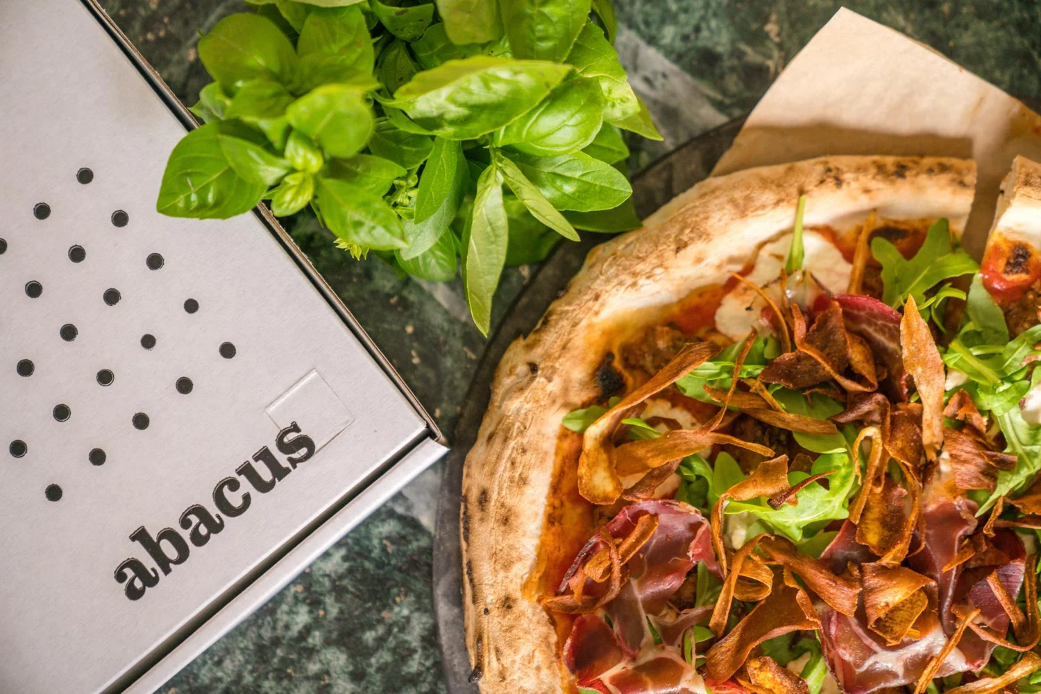 Abacus pizza with fresh basil beside the restaurant's branded menu