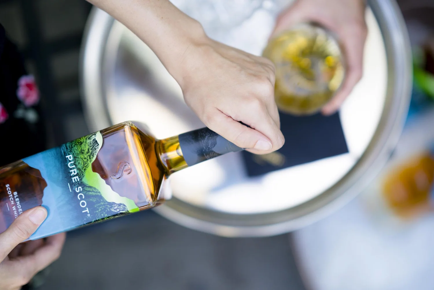 Hand pouring Pure Scot whisky into glasses at an outdoor tasting