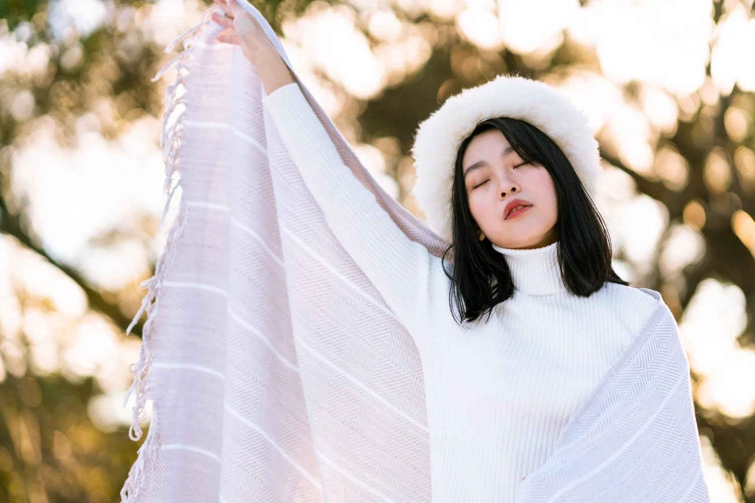 Backlit outdoor portrait of a woman lifting translucent white fabric