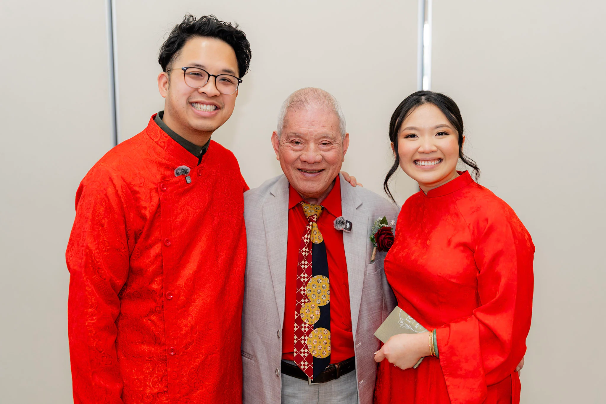 Ron and Joy smiling with a family elder in red ceremonial outfits