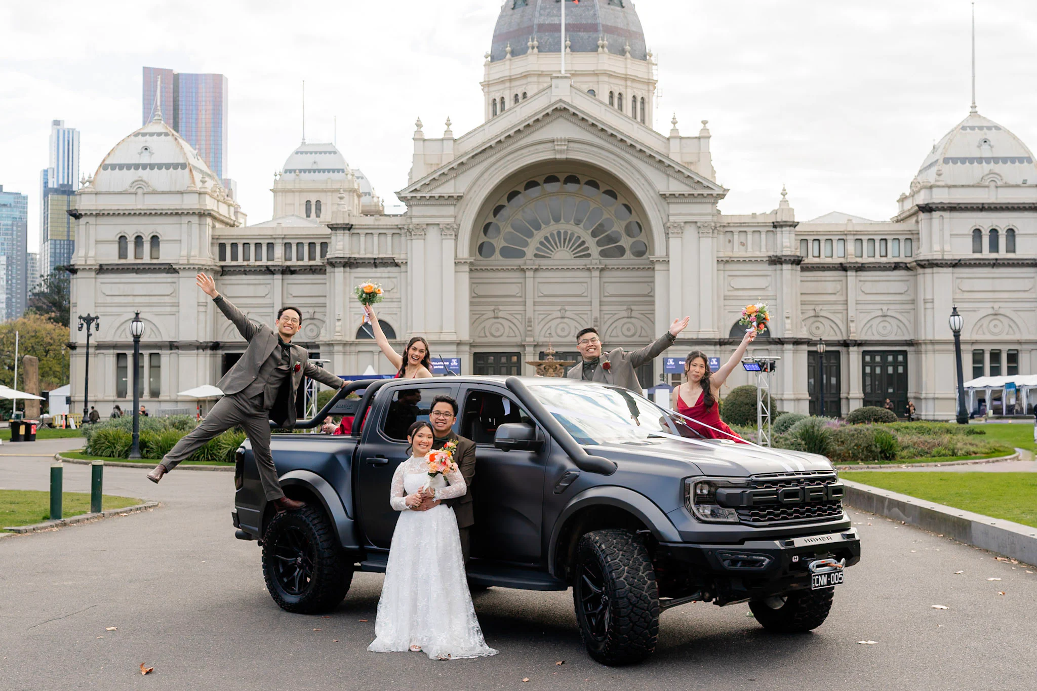 Ron, Joy and their wedding party posing playfully around the black truck