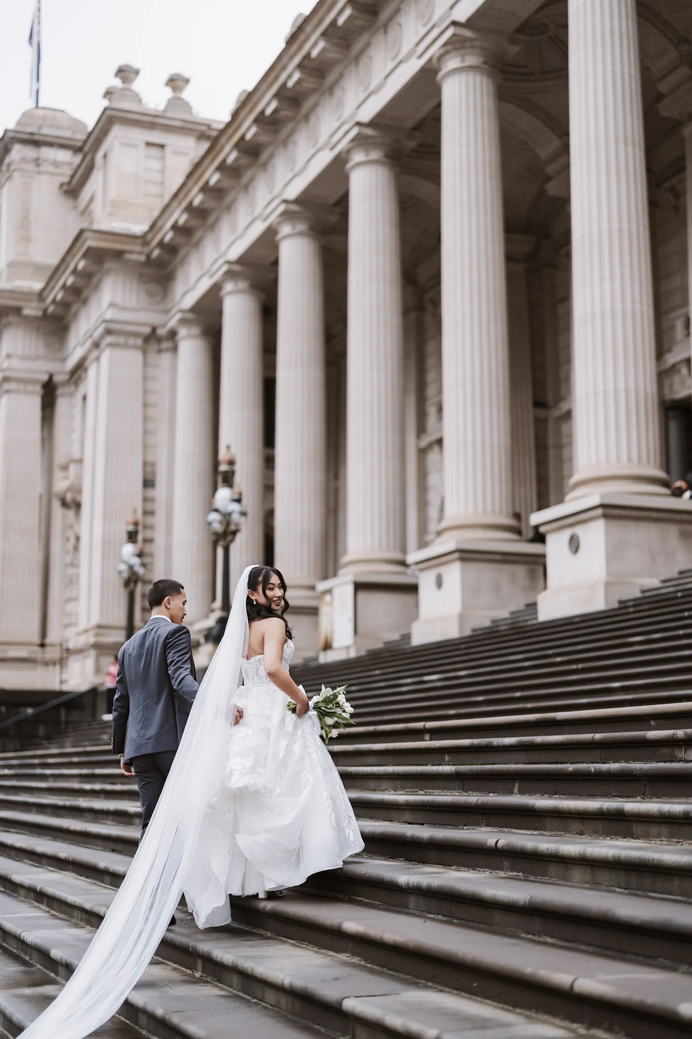 Tee's veil trailing along the grand Melbourne steps beside Kevin