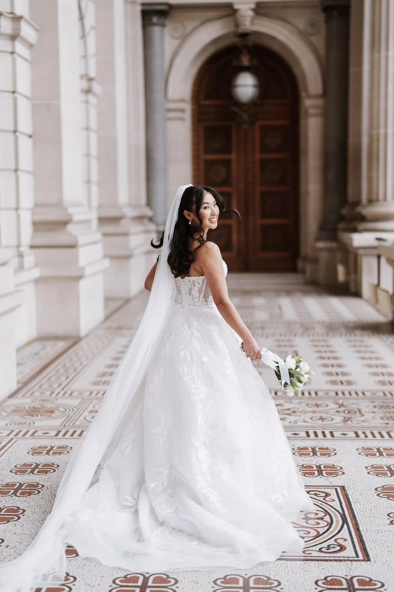 Tee turning in her dress beneath a stone arcade