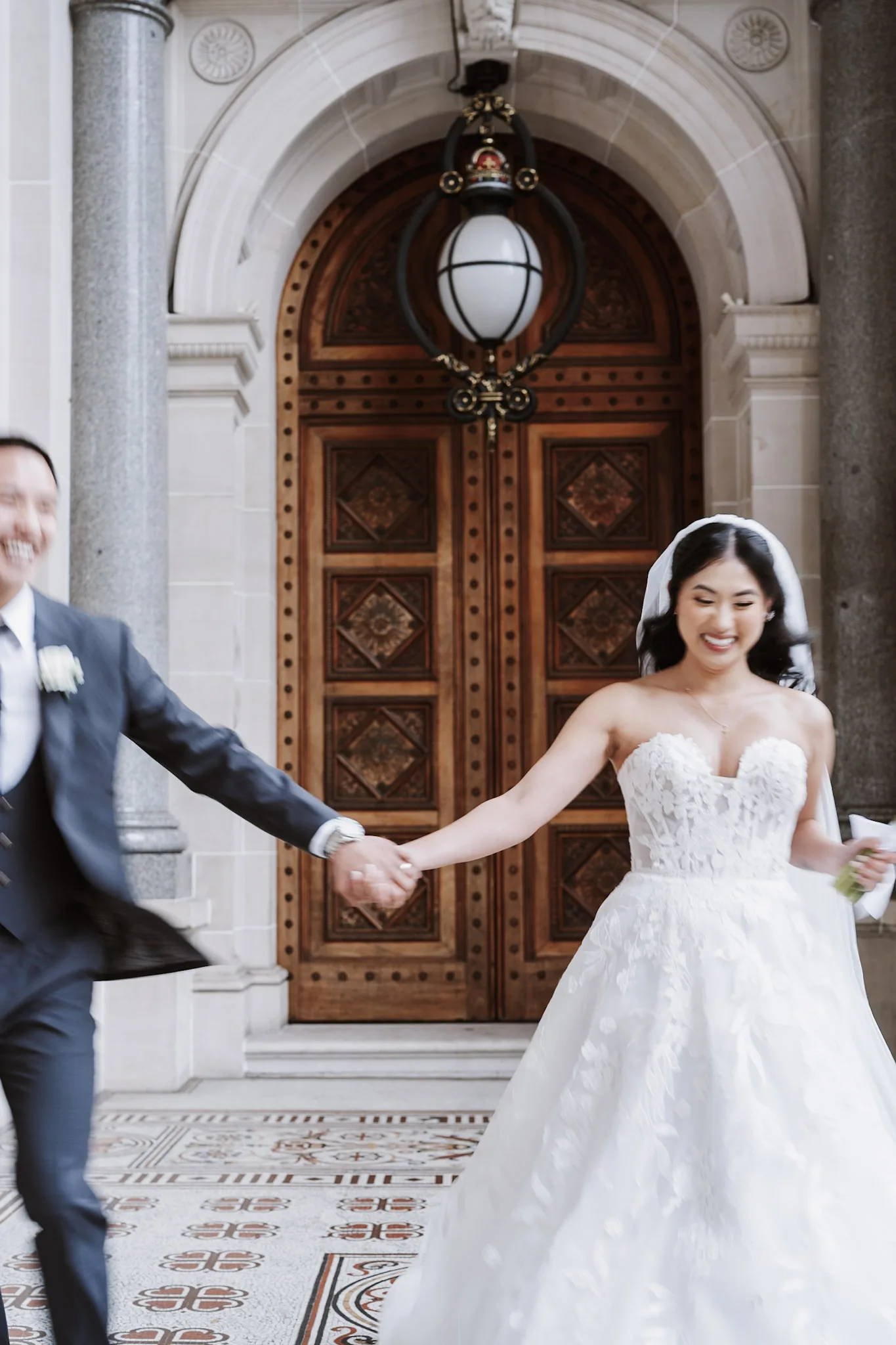 Tee reaching for Kevin's hand with a smile beneath an arched doorway